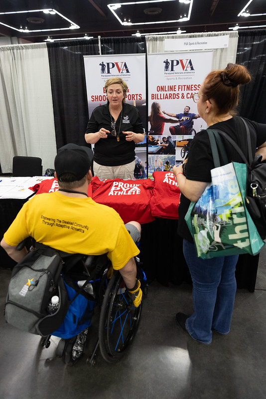 A PVA representative wearing a PVA polo speaks with two attendees of the National Veterans Wheelchair Games