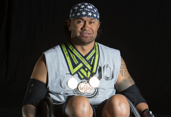 image of Sualauvi posing with his multiple wheelchair games medals